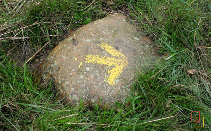 Una flecha amarilla sobre una roca marca el Camino de Santiago, guiando a los peregrinos hacia su destino.